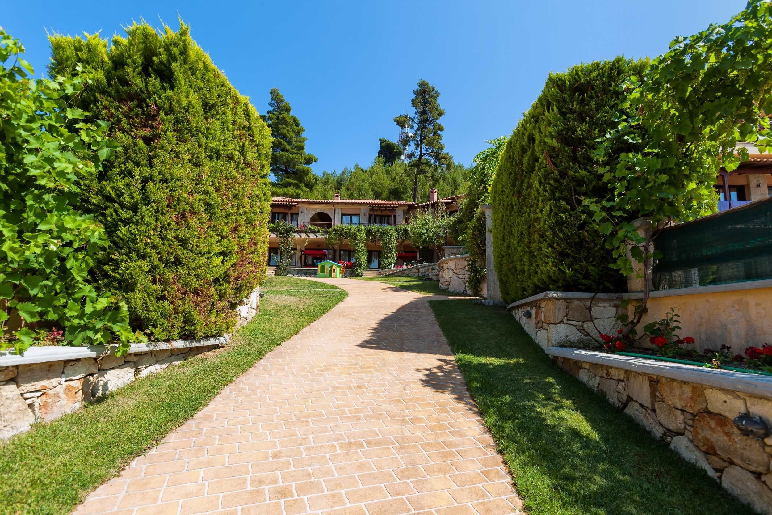 A paved pathway leading to a building surrounded by lush greenery and stone walls.