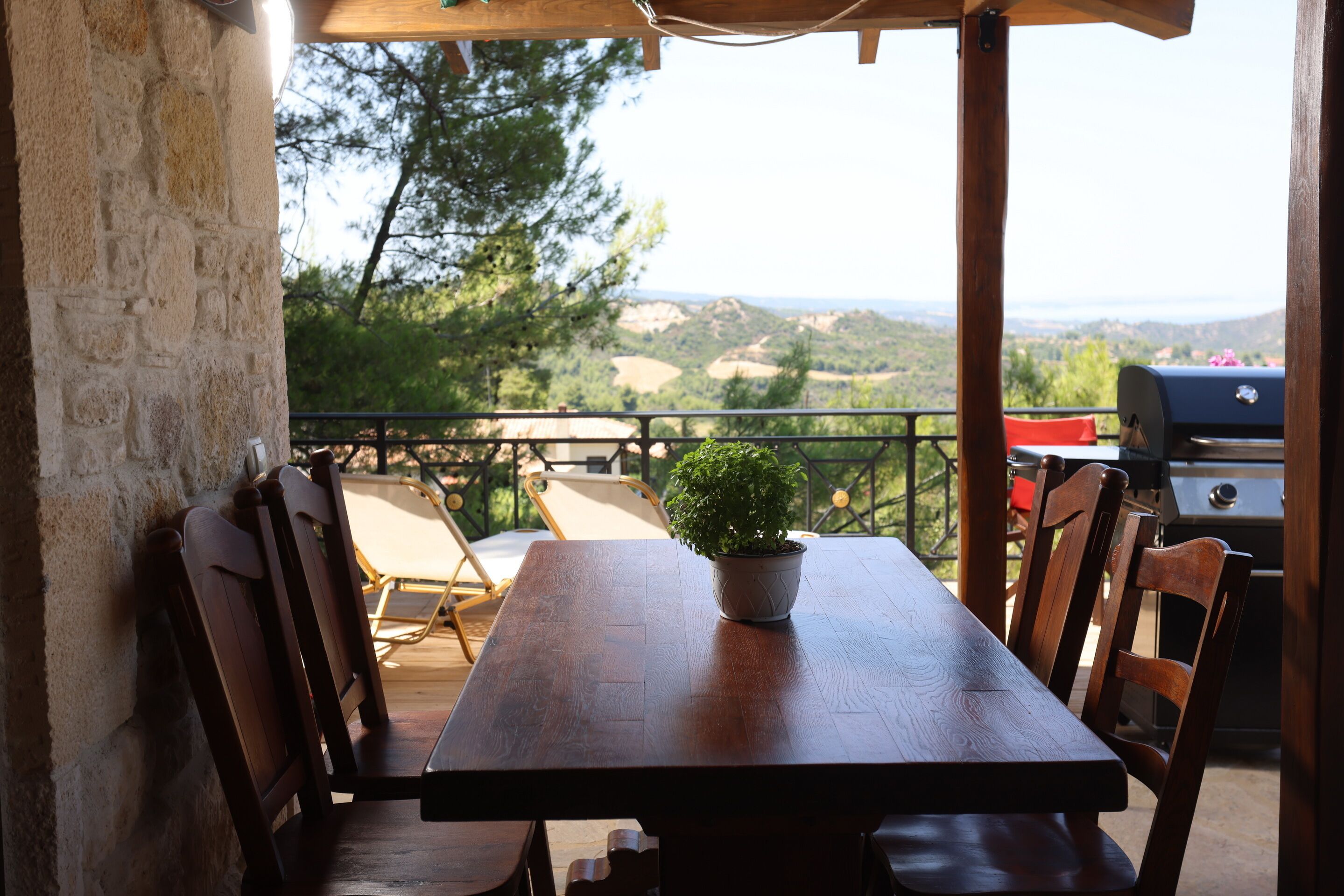 Een houten tafel met stoelen en een bloempot op een balkon met uitzicht op een prachtig landschap.