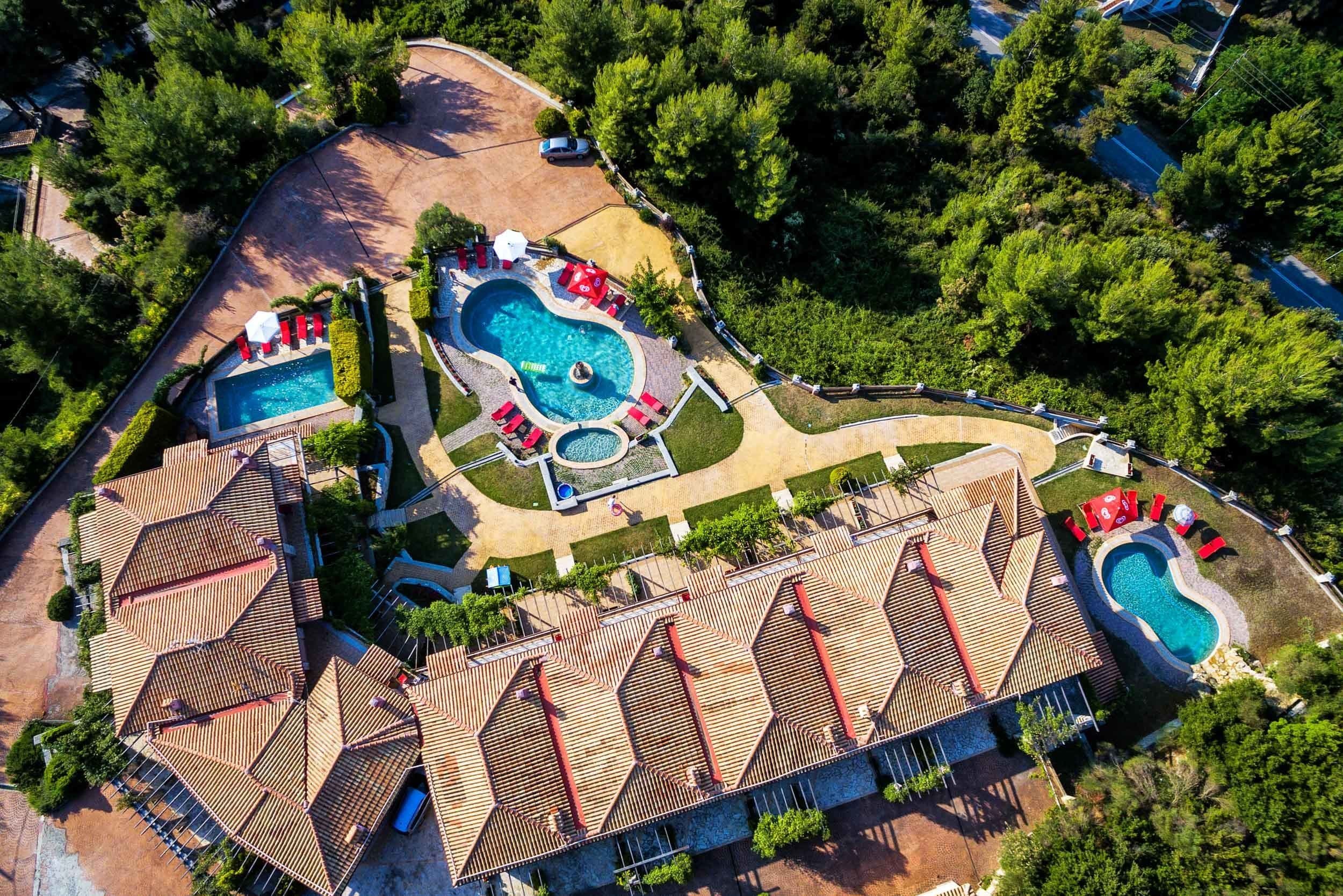 Une vue aérienne d’un complexe hôtelier doté de plusieurs piscines, de chaises longues et d’un grand bâtiment dont le toit se distingue par son architecture particulière.