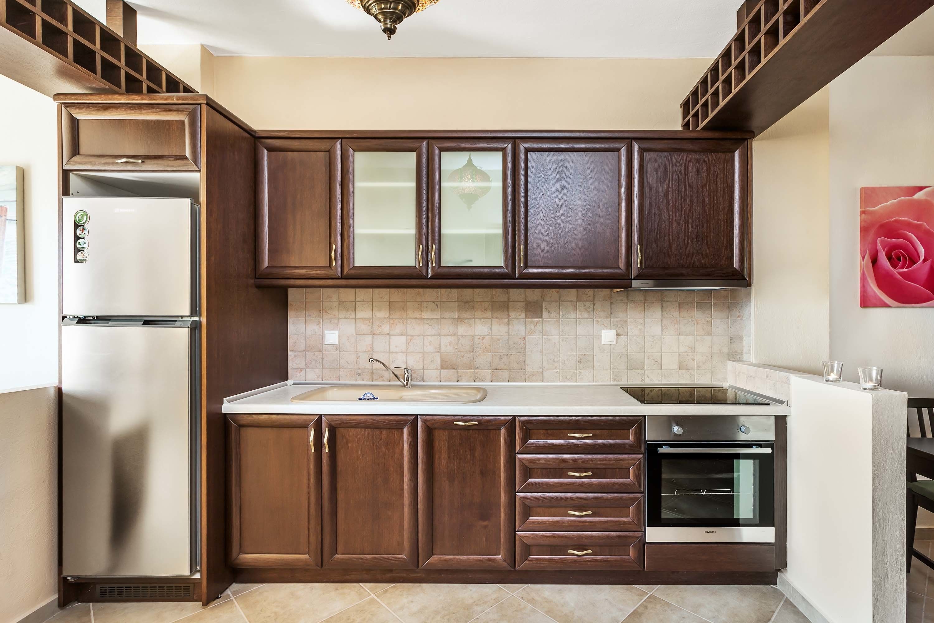 A kitchen with dark wooden cabinets, a stainless steel refrigerator, a built-in oven, and a tiled backsplash.