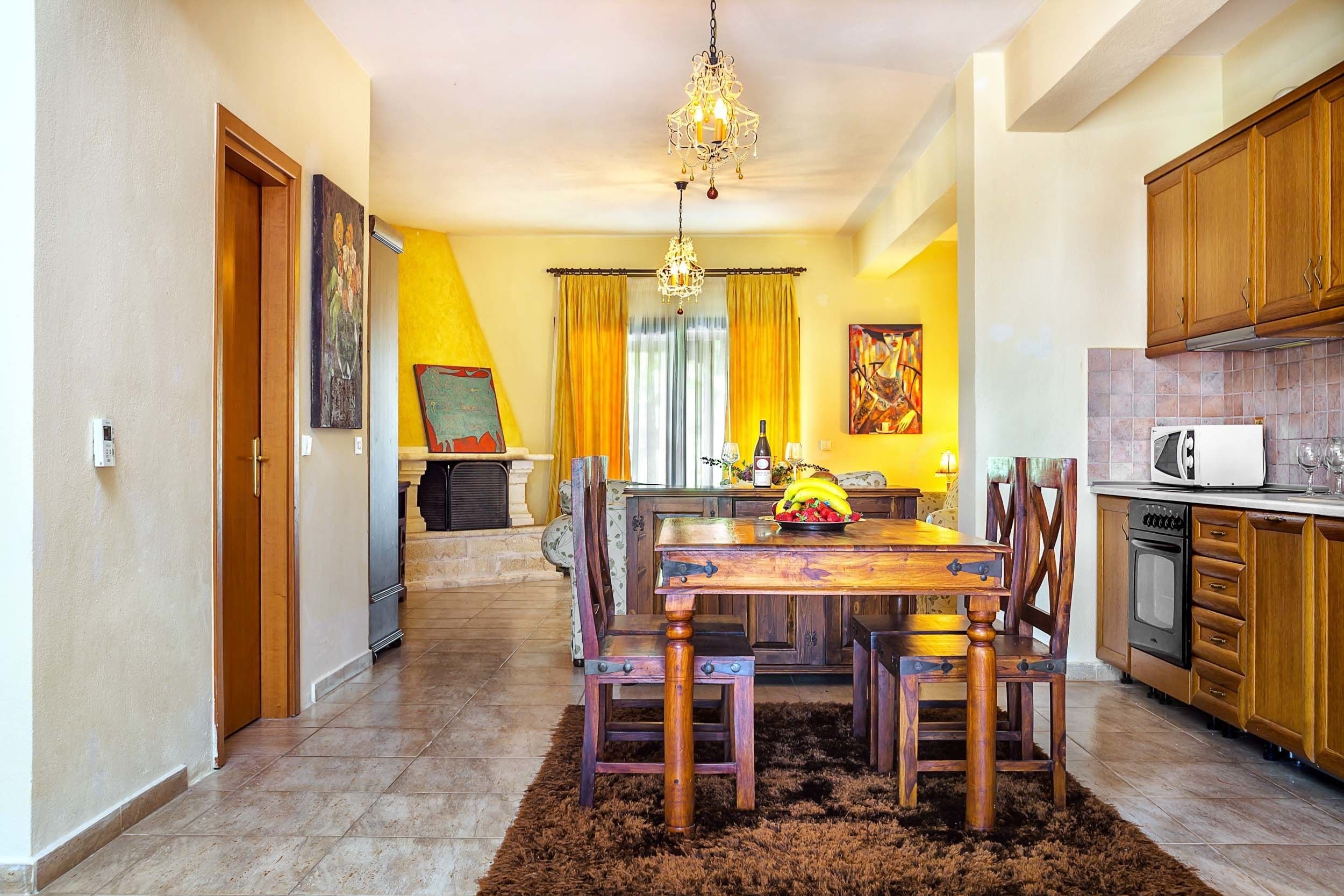 A dining area with a wooden table and chairs, a chandelier, and a kitchen with wooden cabinets.