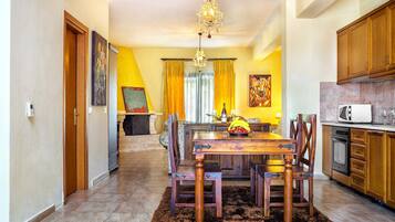 A dining area with a wooden table and chairs, a chandelier, and a kitchen with wooden cabinets.
