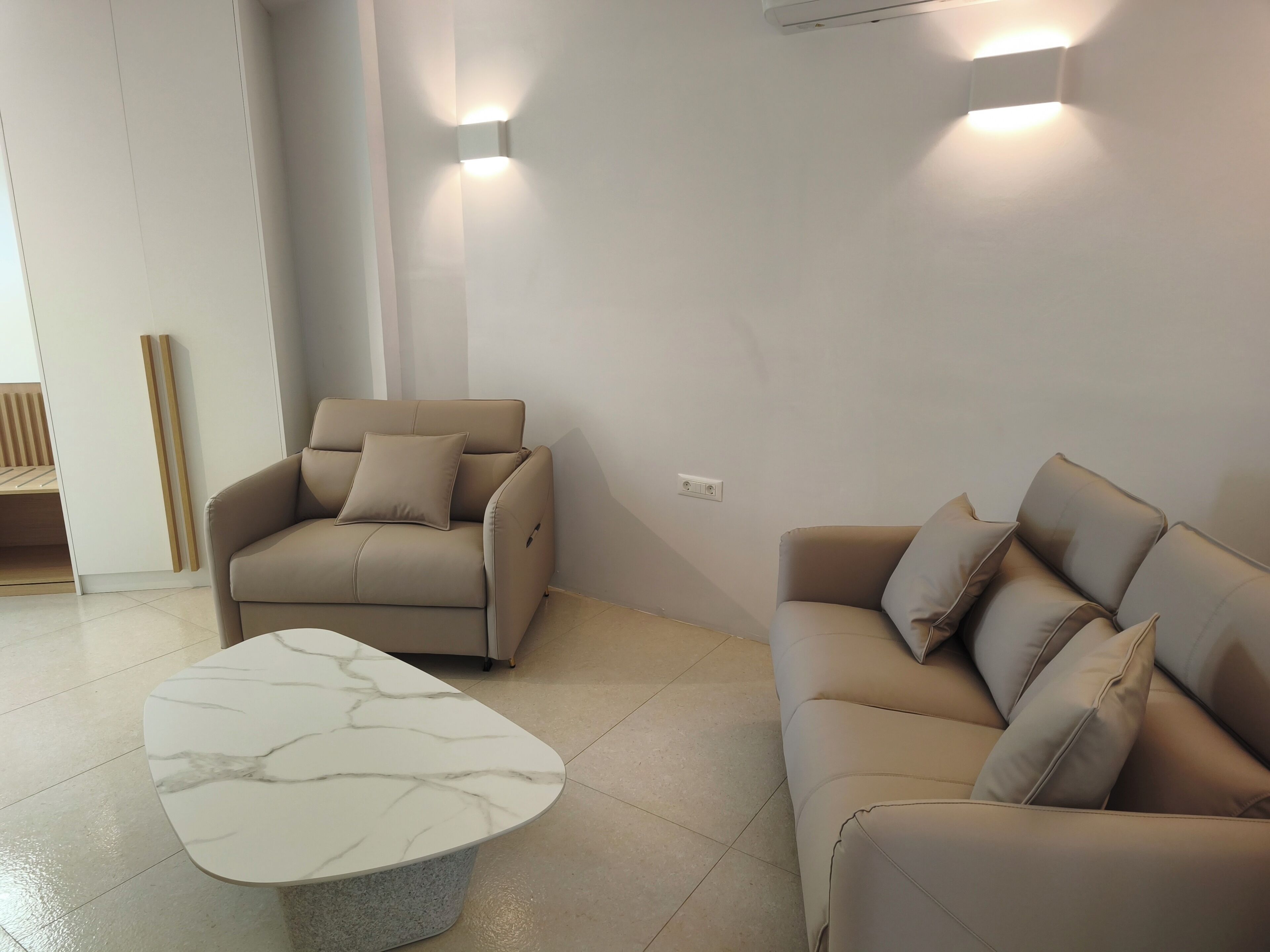 Ein modernes Wohnzimmer mit einem beigen Sofa, einem passenden Sessel und einem Marmortisch.