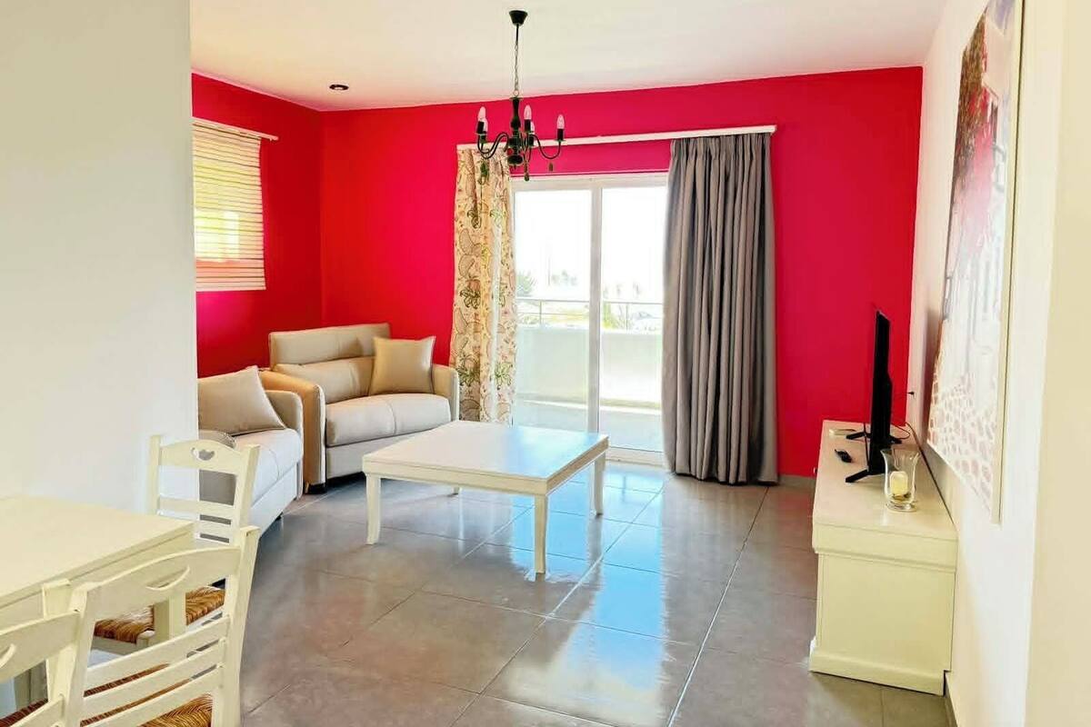 Una sala de estar con sofá, una mesa de centro, televisión y un balcón con cortinas.