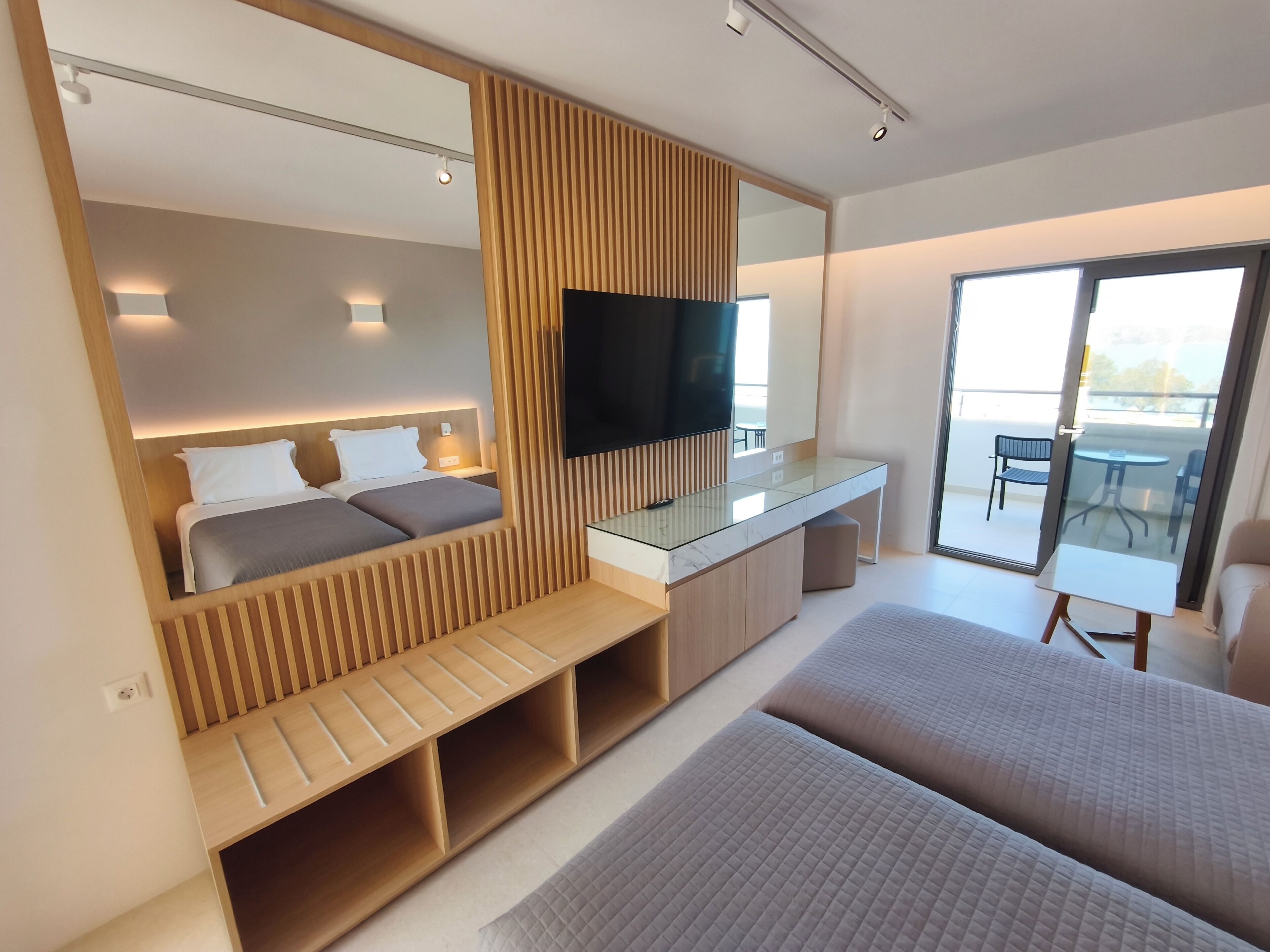 A modern hotel room with a bed, a desk, a TV, and a balcony.