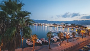 A marina with boats docked, palm trees, and a cityscape in the background. - Kos Palace Hotel (Kos)