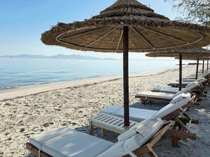Una playa con tumbonas y sombrillas de paja.