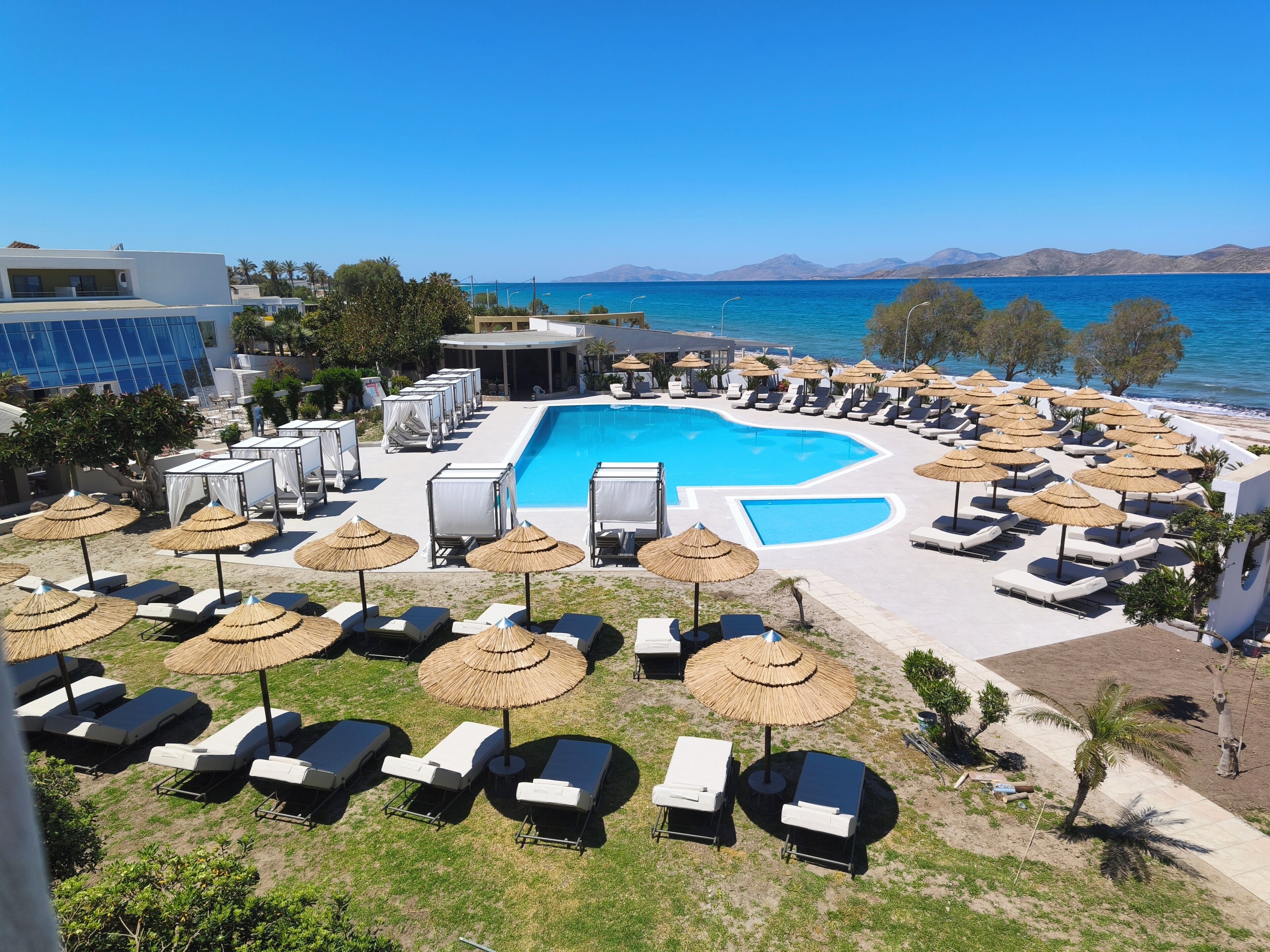Un resort con una piscina grande, sillas de descanso, sombrillas y vistas al mar.