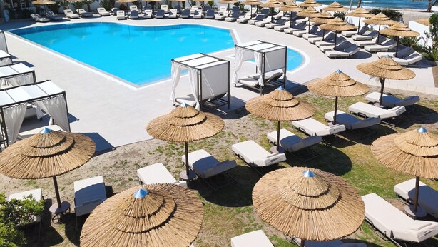 A poolside area with lounge chairs and umbrellas, a swimming pool, and a view of the sea and mountains. - Kos Palace Hotel (Kos)