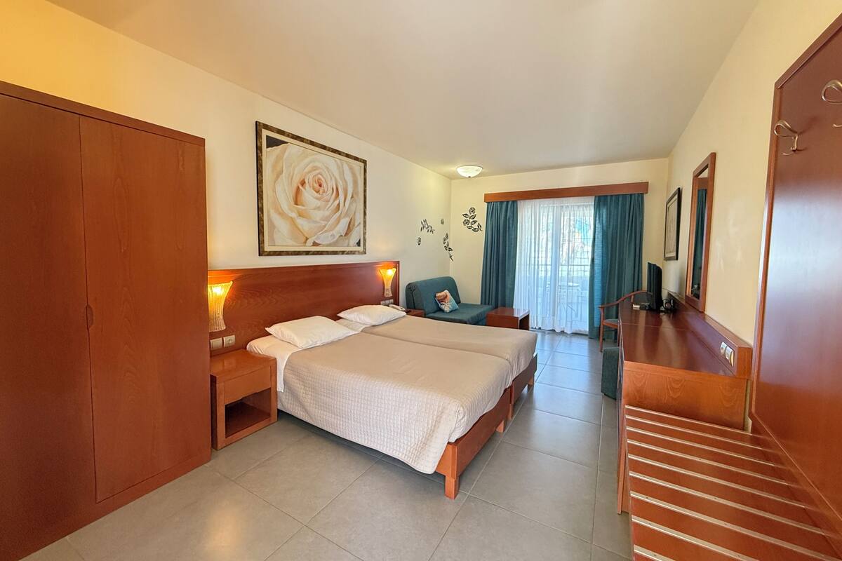 Habitación de hotel con una cama grande, un escritorio, una silla, un armario y vistas al exterior a través de una ventana.