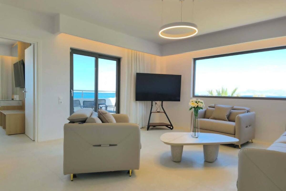 Una sala de estar moderna con un sofá, una mesita de centro, un televisor sobre un mueble bajo y vistas al mar.