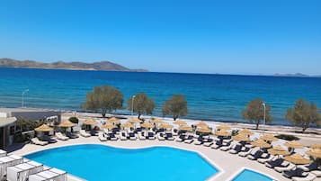 A pool area with lounge chairs and umbrellas, surrounded by a clear blue sky and a view of the sea.