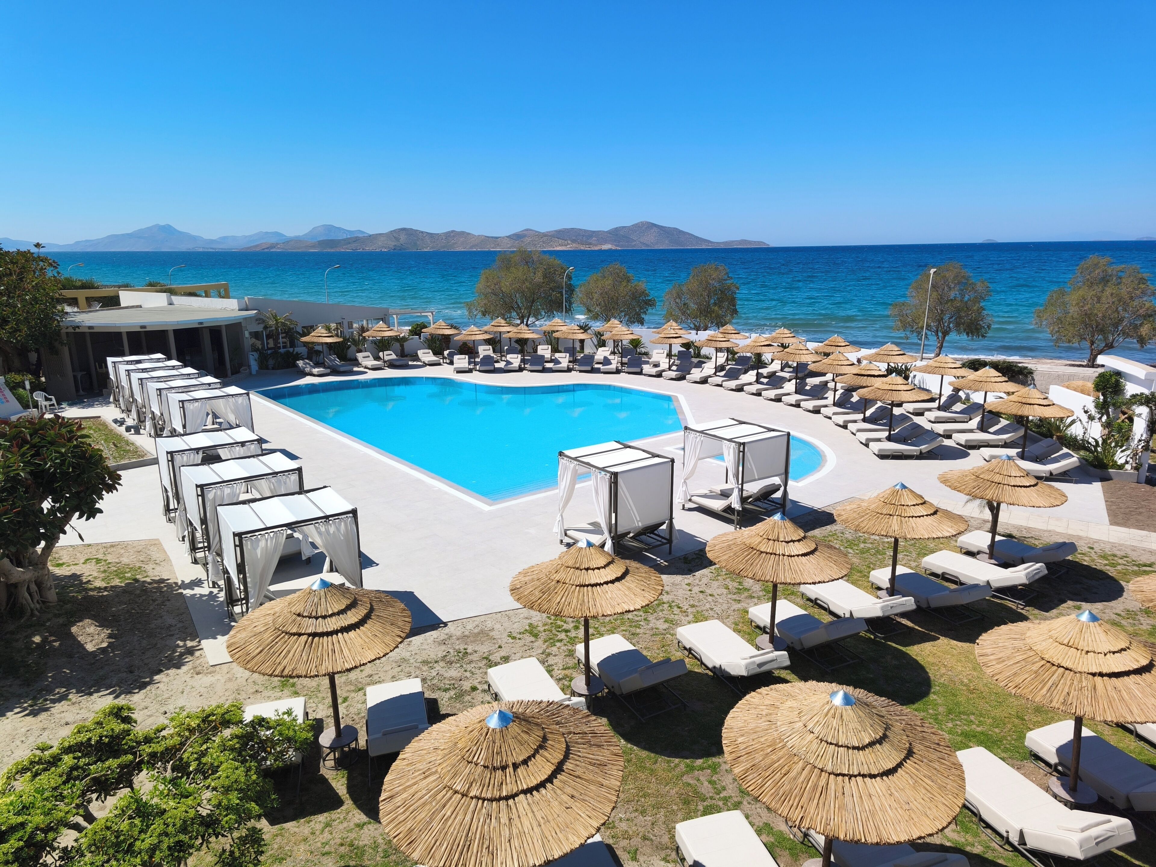 A poolside area with lounge chairs and umbrellas, a swimming pool, and a view of the sea and mountains.