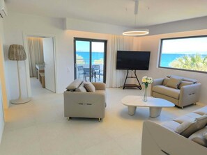 Una sala de estar moderna con sofá, mesa de centro y televisor, con vistas a un balcón que da al océano.
