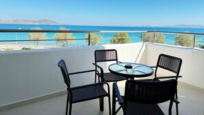 A balcony with a table and chairs, overlooking a coastal view with clear blue sea and distant mountains. - Kos Palace Hotel (Kos)