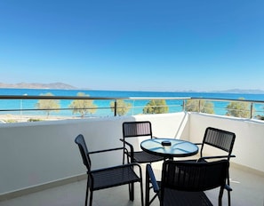 Ein Balkon mit Tisch und Stühlen, der Blick auf die Küste mit klarem, blauem Meer und entfernten Bergen freigibt.
