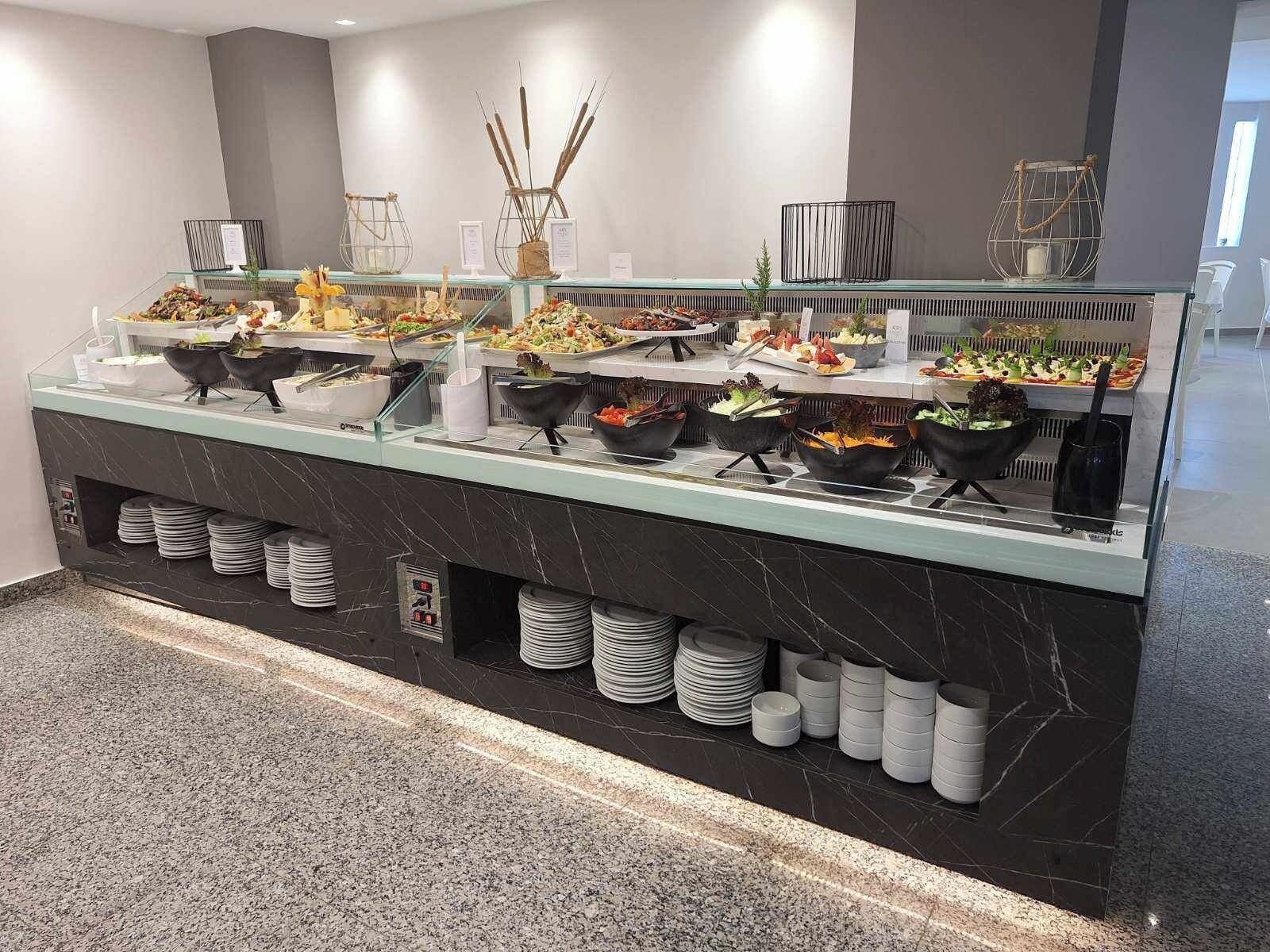 A buffet setup with various food items and utensils, arranged on a marble counter with glass display cases.