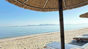 Una playa con sillas de descanso y una sombrilla de paja.