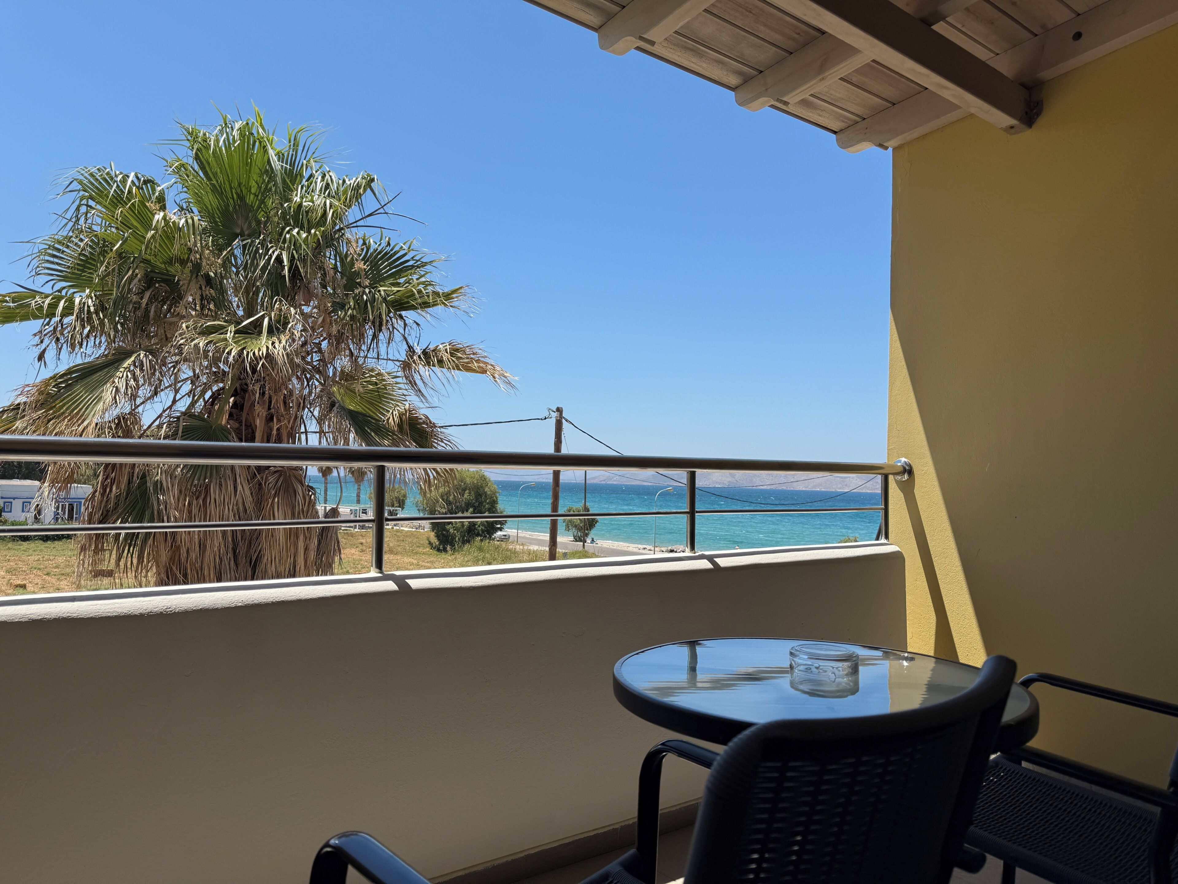 Un balcón con vista al mar, una palmera y una mesa con una silla.