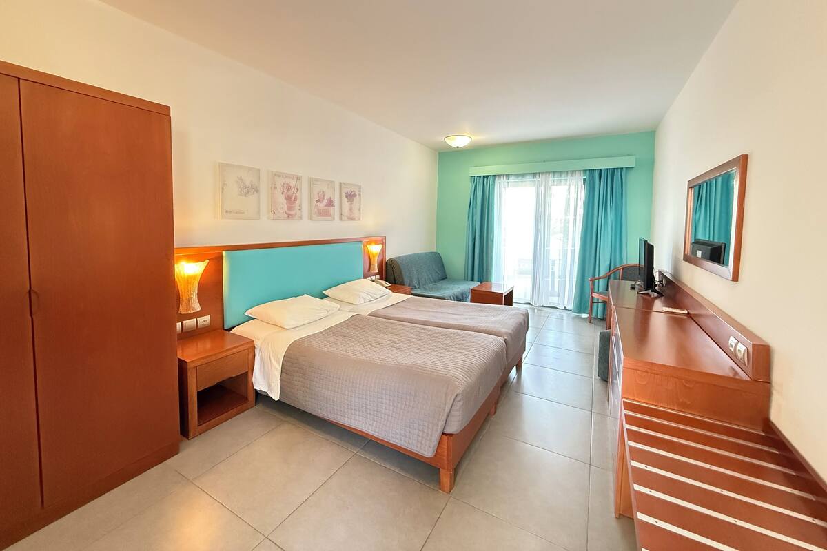 Habitación de hotel con dos camas, un escritorio, una silla, un televisor y un armario.