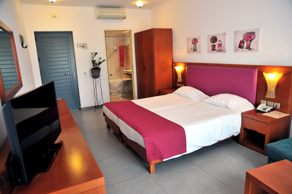 A hotel room with a bed, a TV, a wardrobe, a bathroom, and artwork on the wall.