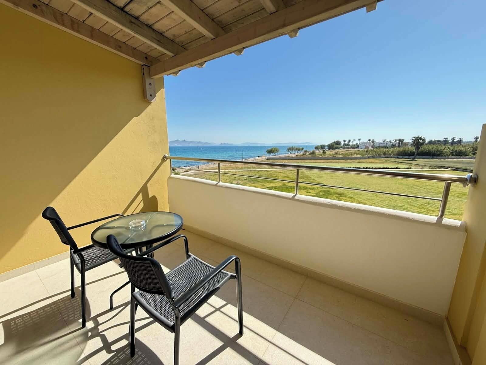 Un balcón con mesa y sillas, vista al mar y una zona con césped.