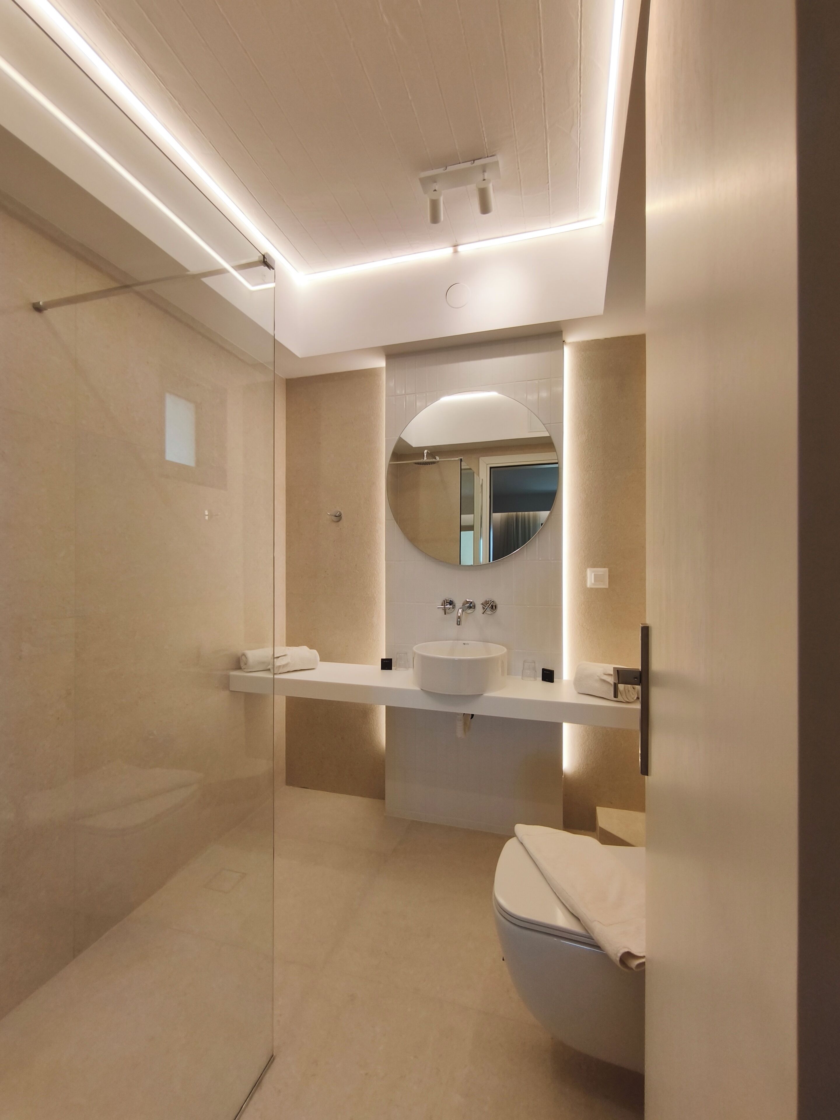 Une salle de bain moderne avec une douche à parois de verre, un miroir rond, un lavabo blanc et des toilettes.