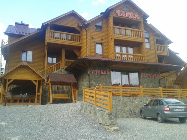 A wooden hotel with balconies, a restaurant, and a car parked in front. - Charda Hotel (Bukovel)