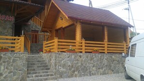 Una cabaña de madera con fachada de piedra, balcón de madera y techo rojo.