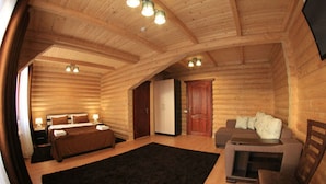 Interior de una cabaña de troncos con una cama, un sofá, un televisor y una chimenea.