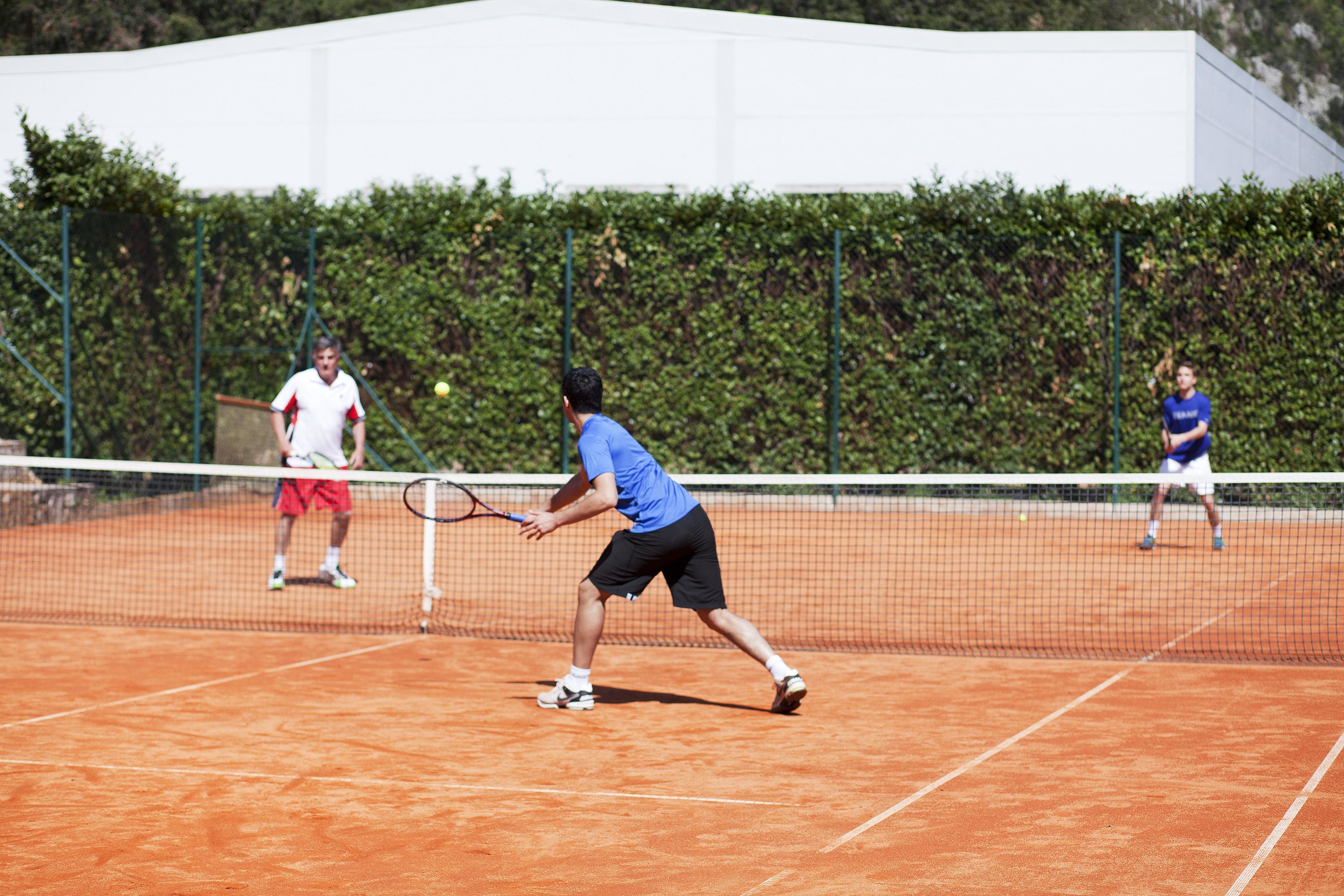 Una cancha de tenis con una red en el centro, rodeada por un seto.