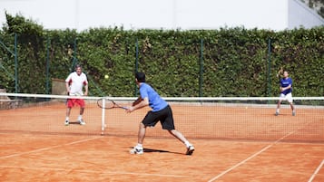 Una cancha de tenis con una red en el centro, rodeada por un seto.