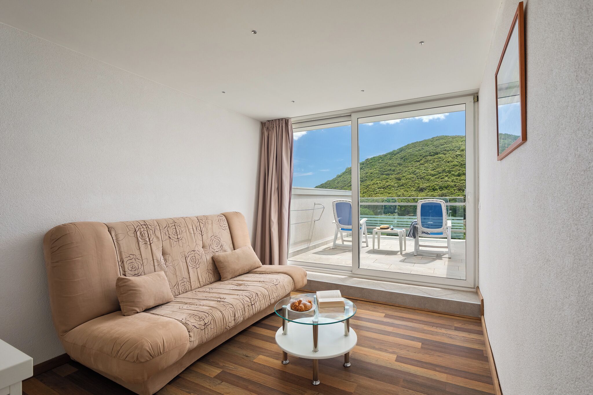 Een moderne woonkamer met een bank, een glazen salontafel en een balkon met tuinmeubilair.