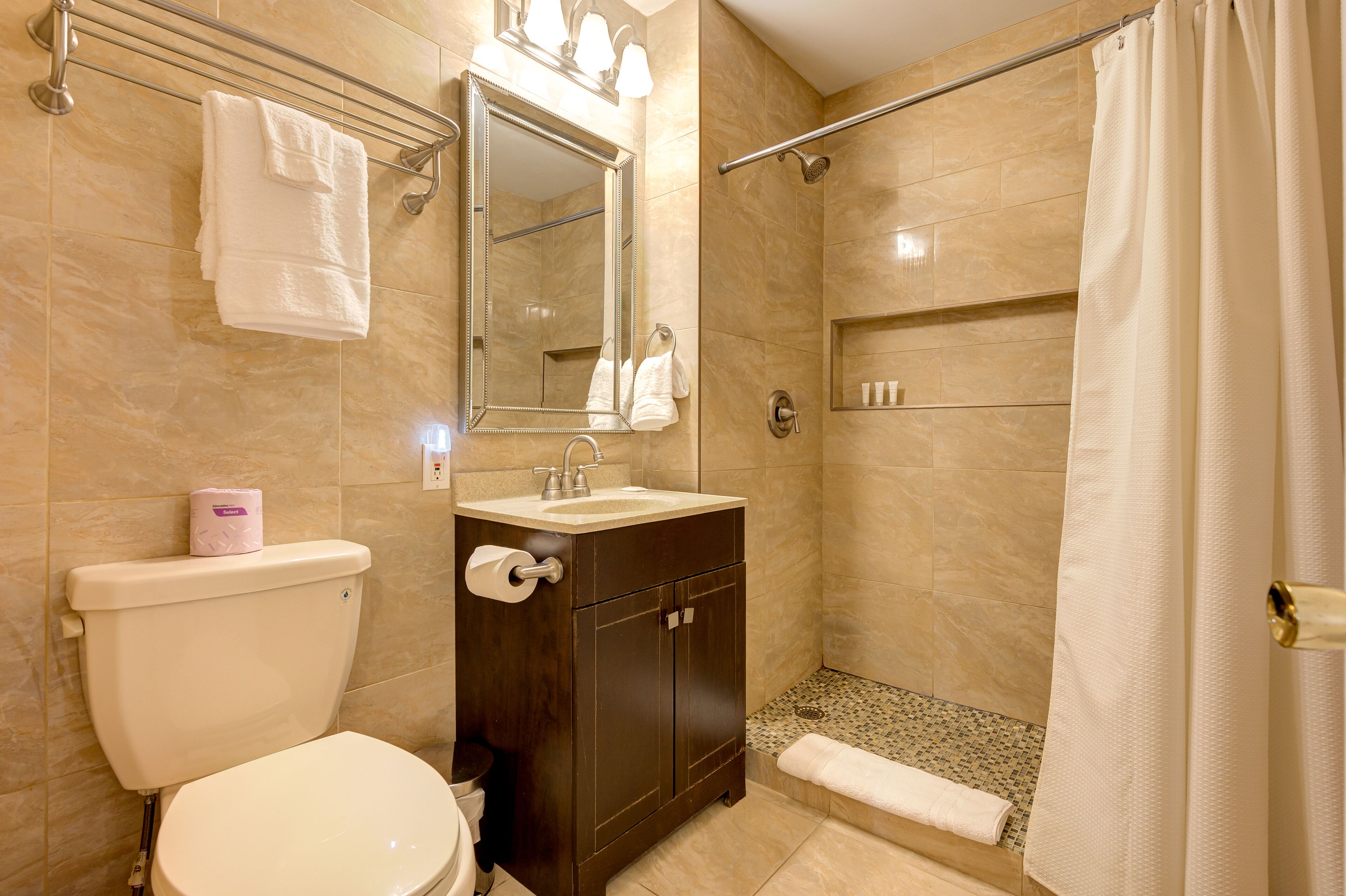 Un baño con inodoro, lavamanos, espejo, ducha y perchero para toallas.