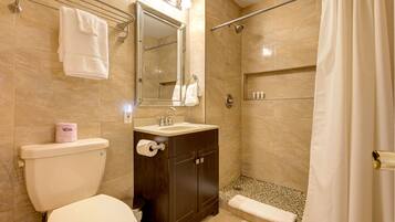 Un baño con inodoro, lavamanos, espejo, ducha y perchero para toallas.