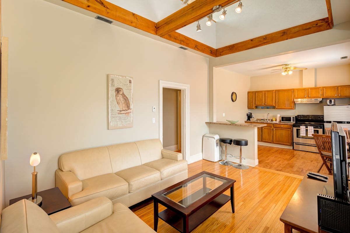 A modern living room with a sofa, a glass coffee table, and a kitchen in the background.