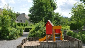 Un parque infantil con una estructura de juego roja y amarilla, rodeado por una valla de madera y suelo de grava.