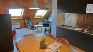 Una habitación acogedora con techo de madera, una mesa de comedor con sillas, un televisor pequeño y una kitchenette con fregadero.