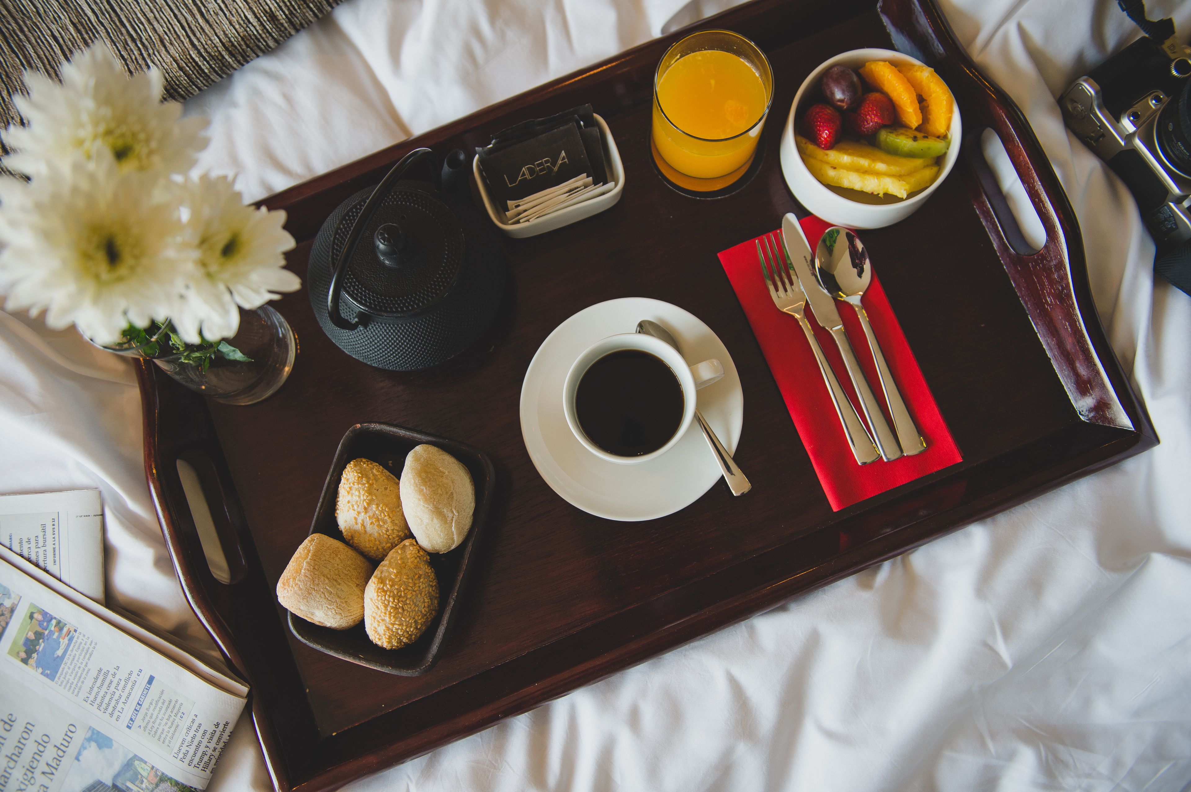 Ontbijtkarretje met een kop koffie, een schaal fruit en broodjes op een bed.