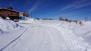 Una carretera cubierta de nieve que conduce a un edificio con un cartel que indica que es un hotel, restaurante y centro de alquiler de esquíes.