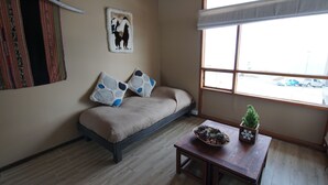 Una habitación con un sofá, una mesita con una planta y una ventana con vistas a coches aparcados.