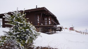 Una cabaña de madera con balcón, rodeada de nieve y un pequeño abeto.