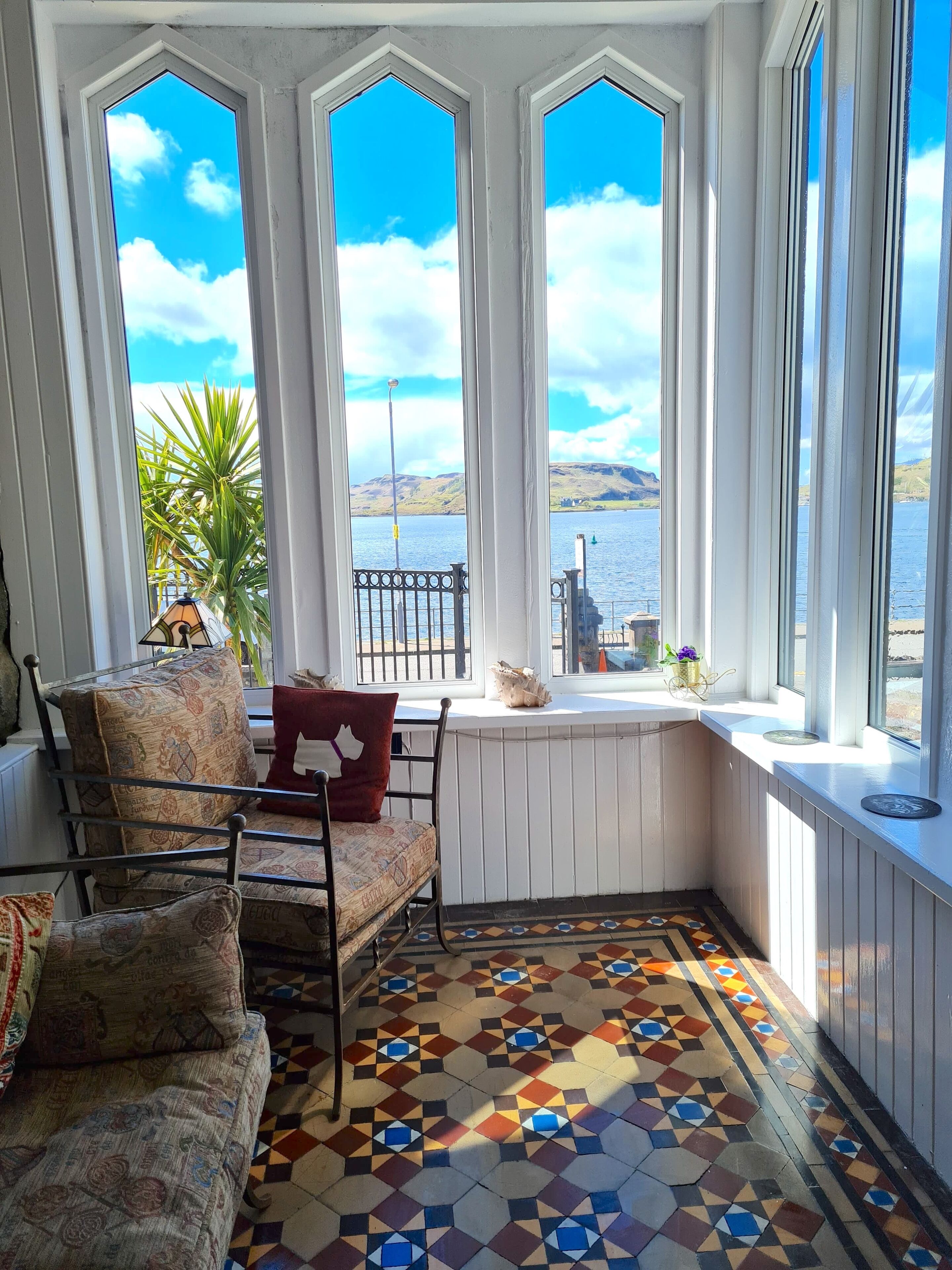 A cozy corner with a patterned sofa, a small table, and a view of a lake through large windows.