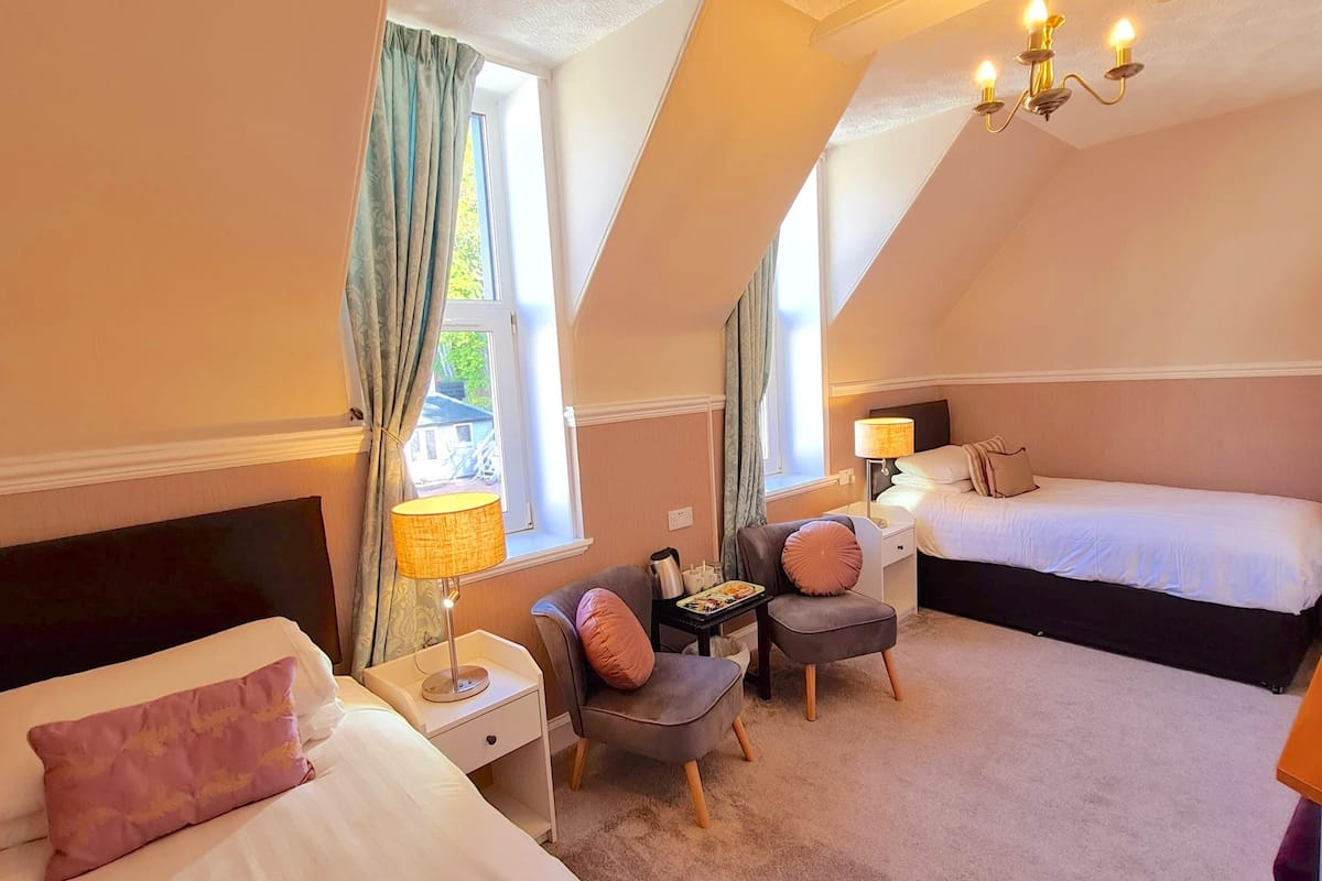 A hotel room with two beds, a desk, a chair, and a lamp.