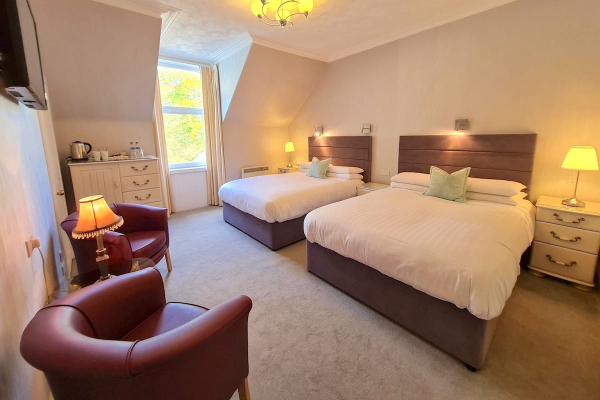 A bedroom with two beds, a desk, a chair, and a window.