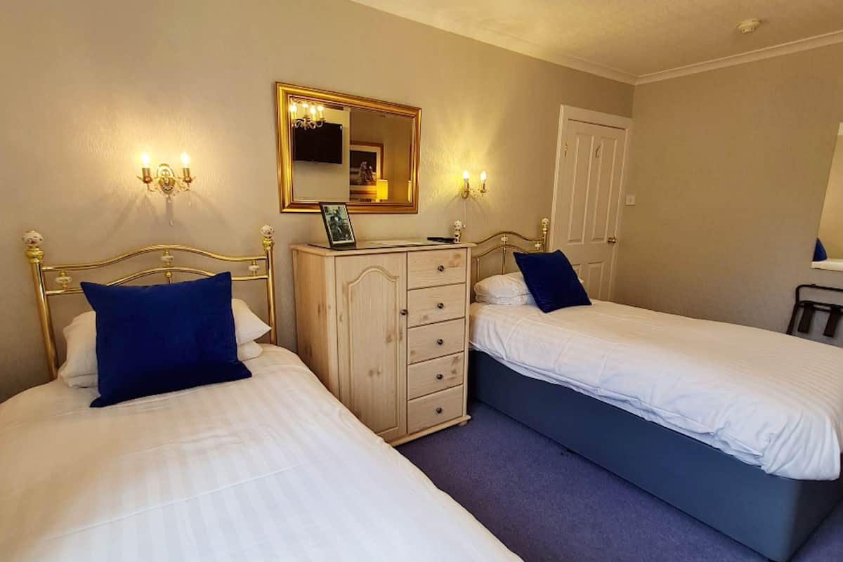 A hotel room with two single beds, a wooden dresser, a mirror, and wall sconces.