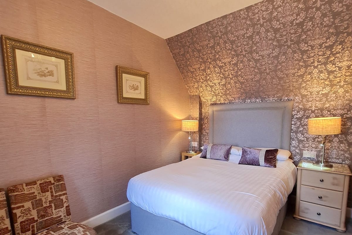 A bedroom with a large bed, two bedside tables with lamps, a chair, and a chandelier.