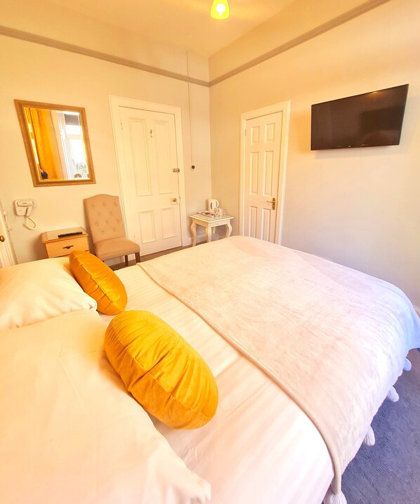 A hotel room with a large bed, two chairs, a small table, a TV, and two doors. - Corriemar Guest House (Oban)