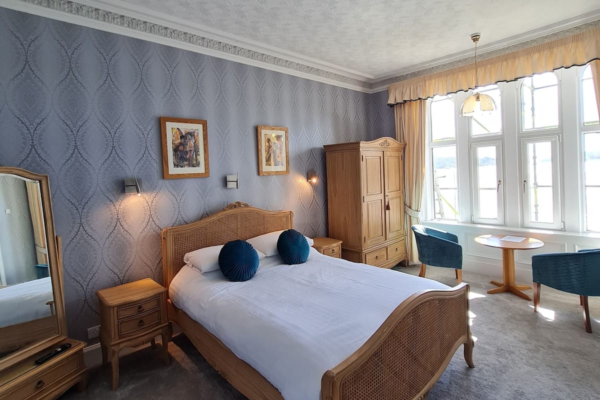 A bedroom with a large bed, wooden headboard, two bedside tables, a wardrobe, and a window with curtains.