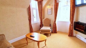 A cozy living room with a sofa, a wooden coffee table, a patterned armchair, and a television. - Corriemar Guest House (Oban)
